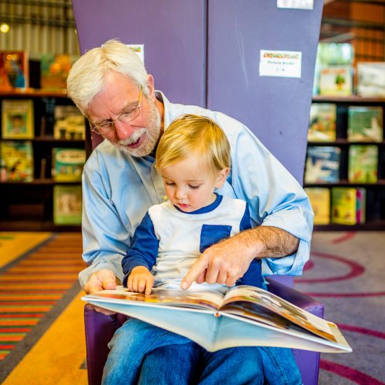 Grandfather Teaches Grandson to Read at Library Grandfather Teaches Grandson to Read at Library
